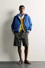Cazadora técnica relaxed fit de color azul, con cuello subido, capucha ajustable, bolsillos frontales de plastrón con solapa, cierre de cremallera oculta y puños elásticos.