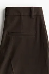 Pantalón sastrero de corte amplio con pinzas, cierre frontal con botón y corchete ocultos, bolsillos laterales al bies y bolsillos decorativos traseros.