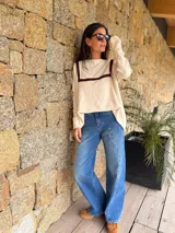 Sweater de punto color beige con corte holgado, cuello redondo y detalles de apliques en cuero marrón en la parte frontal. Presenta mangas largas y una textura suave.