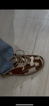 Zapatillas bajas de cuero con estampado de vaca en blanco y marrón.