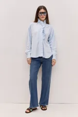 Camisa celeste con cuello alto, volados frontales y mangas largas con puños ajustados.