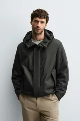Parka de tejido técnico con acabado engomado, cuello subido y capucha ajustable. Presenta cierre frontal con cremallera oculta bajo solapa con botones a presión, bolsillos laterales de vivo y mangas largas con puños ajustables.