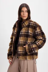 Campera de corderito sintético con diseño a cuadros en tonos marrones y negros. Presenta cuello alto, cierre frontal completo y detalles de paneles en color marrón liso. El diseño es de silueta holgada, largo tipo crop y cuenta con un cordón elástico ajustable en el ruedo.