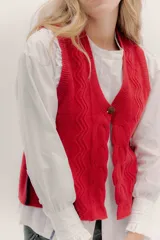 Chaleco de tejido de punto color rojo, con escote en V y un botón de madera en el centro. Presenta un patrón de zigzag en relieve a lo largo de toda la prenda.