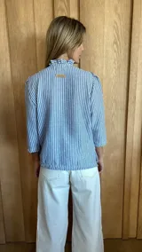 Camisa de manga tres cuartos color beige con cuello con volados y botones frontales. Presenta un detalle de color negro en la parte superior de las mangas.