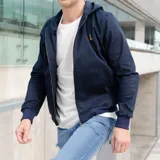 Campera azul marino de gabardina con capucha, cierre frontal con cremallera, puños y cintura acanalados y un pequeño logo bordado en el pecho.