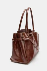 Bolso marrón formato city, confeccionado en piel. Tiene doble asa de mano, bolsillos exteriores (uno con cierre imantado) y doble compartimento interior con cierre de botón imantado. Incluye bolsillos interiores con cremallera.