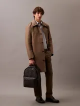 Mochila Calvin Klein con estampado integral de monograma CK en tonos oscuros. Cuenta con un compartimento principal amplio, bolsillo frontal con cierre, asa superior y compartimento interno para laptop.