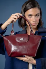 Cartera de mano tipo shopper pequeña, color bordó, confeccionada en cuero liso con solapa frontal y cierre metálico con logo grabado.