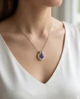 Collar de plata con cadena fina y dije circular que presenta una circonia central en color violeta rodeada por pequeñas piedras brillantes.