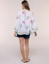 Kimono de poliéster blanco con diseño abierto, mangas amplias y bordados coloridos de motivos florales y arabescos, con terminaciones en ondas de hilo verde.