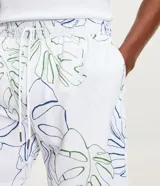 Bermuda de baño blanca con estampado floral de hojas de costilla de Adán en negro. Tiene cintura elástica con cordón ajustable y bolsillos laterales.