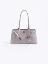 Cartera de hombro color gris, confeccionada en cuero vacuno descarne. Presenta un diseño estructurado con cierre de torniquete metálico y detalle de llavero colgante con candado y llave. Cuenta con doble asa fija.