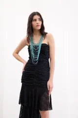 Vestido largo negro strapless de encaje con frunces en el torso, falda asimétrica en capas con volados y breteles removibles.