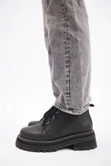 Borcego de cuero color gris con cordones color naranja, suela track negra de goma y detalle de gamuza en la parte superior del tobillo.