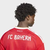 Camiseta de fútbol Adidas del FC Bayern, modelo local, color rojo con rayas verticales sutiles, detalles en blanco y dorado en el cuello y las mangas, y el logo del patrocinador en el pecho.
