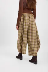 Pantalón de corte holgado con silueta tipo balloon, confeccionado en tela a cuadros. Presenta cintura elástica con cordón ajustable y cortes laterales circulares que aportan volumen a la prenda.