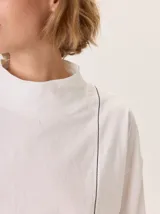 Remera blanca de manga larga con cuello alto, corte holgado y costuras verticales decorativas en el frente.