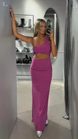 Vestido largo fucsia brillante con corte asimétrico de un solo hombro, aberturas en la cintura y falda larga ajustada con fruncido en un lateral.