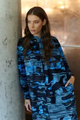 Vestido camisero largo con estampado geométrico en tonos camel y negro. Cuenta con mangas largas con puños, un bolsillo frontal amplio, botones frontales y un botón de cierre en el cuello.