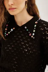 Sweater negro de punto calado con cuello polo decorado con apliques de piedras brillantes de colores. Presenta mangas largas con puños ajustados y un diseño elegante.