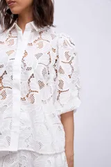 Camisa blanca de broderie con cuello clásico, mangas abullonadas 3/4 y cierre frontal con botones.