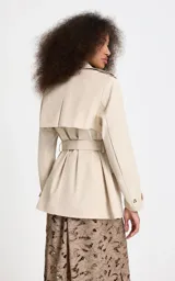 Trench corto Le Lis Blanc modelo Georgia, color beige, de corte recto, con cuello con solapa, doble botonadura frontal con botones carey, bolsillos delanteros con solapa y cinturón ajustable para la cintura.