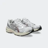 Championes Asics modelo Gel 1130, color blanco con detalles plateados y verde oscuro. Diseño retro inspirando en el running con tecnología GEL en el talón.