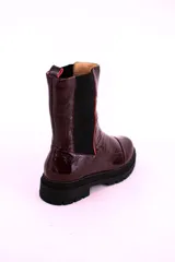 Bota tipo chelsea de cuero acharolado color bordó, con elásticos laterales negros y suela track dentada.