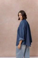 Camisa de denim azul con bordados florales en tonos amarillos y celestes sobre los hombros y el pecho. Presenta cuello clásico, cierre frontal con botones y mangas largas con puños.