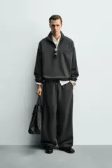 Sudadera de corte relajado color negro, con cuello alto y cierre frontal de cremallera. Presenta un bolsillo de vivo en el pecho con un estampado a contraste y acabados elásticos en puños y ruedo.
