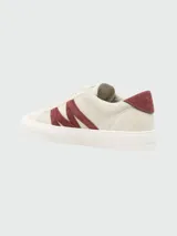 Zapatillas bajas Moncler modelo Moncado2, color crema, con franjas laterales en gamuza color bordó que forman una 'M' y la palabra 'MONCLER' grabada. Tienen cordones grises y suela de goma blanca.