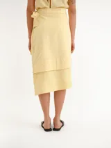 Pollera midi color amarillo claro, tipo envolvente (wrap), con diseño asimétrico en capas y lazo lateral para anudar.