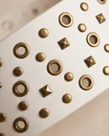 Cinto ancho de símil cuero color blanco con diseño de múltiples tachas metálicas doradas y hebilla metálica redonda en tono bronce.