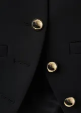 Chaqueta corta negra de cuello alto mao, con cierre frontal cruzado de botones dorados metálicos, hombreras estructuradas y mangas largas con botones en los puños.
