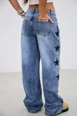 Pantalón de jean tiro medio con corte recto y holgado, presenta bordados de estrellas oscuras a lo largo de los laterales externos.