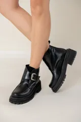 Bota corta de cuero negro con suela track dentada y taco cuadrado. Presenta una tira decorativa en el empeine con una hebilla metálica plateada y tirador en la parte trasera.