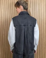 Chaleco de denim color marrón, confeccionado en 100% algodón, con bolsillos frontales amplios, cierre de botones y costuras decorativas bordadas en blanco en los bordes y los bolsillos.