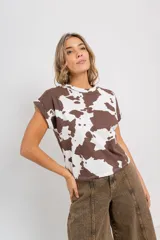 Remera de corte recto y oversize, confeccionada en algodón y elastano. Presenta un estampado de manchas de vaca en tonos marrón y blanco, y mangas con doblez en el borde.