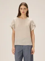Blusa de lino color beige, de corte recto, con cuello redondo y mangas cortas con detalles de volados superpuestos.