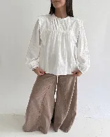 Blusa de algodón color beige con cuello redondo, mangas largas abullonadas con puños elásticos, detalles de puntilla y bordados florales en el frente.