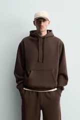 Sudadera con capucha de corte relajado, confeccionada en tejido de algodón con interior perchado. Presenta mangas largas, bolsillo frontal tipo canguro y terminaciones en rib.
