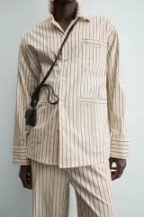 Camisa de calce relajado con diseño de rayas verticales, cuello bowling y manga larga. Cuenta con cierre frontal de botones y tres bolsillos de plastrón: uno en el pecho y dos en la cadera.