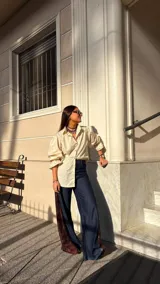 Camisa de color camel con cuello clásico, cierre frontal con botones de madera y mangas largas abullonadas con puños ajustables. Presenta una silueta relajada y versátil.