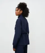 Campera rompevientos azul marino con cuello alto ajustable, cierre frontal y cordones en la cintura para un ajuste entallado. Presenta detalles de costuras en contraste blanco y puños elásticos.