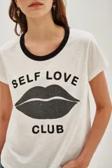 Remera de algodón color blanco con cuello redondo en contraste negro. Presenta un estampado frontal con la frase 'Self Love Club' y un diseño de labios en color negro.