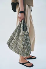 Bolso tipo shopper de tejido con diseño de cuadros en tonos verdes, blancos y marrones, decorado con apliques brillantes. Cuenta con asa de hombro ajustable en material sintético negro, cierre mediante botón imantado y bolsillo interior con cremallera.