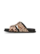 Sandalias planas con tiras cruzadas de pelo con estampado animal print tipo vaca en tonos blancos y marrones, con suela negra.