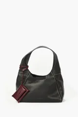 Cartera de cuero vacuno color negro, con costuras a contratono en color blanco y un práctico bolsillo frontal desmontable en color bordó con tiras envolventes. Cuenta con asa para el hombro.