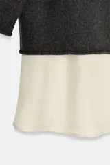 Jersey de punto color gris oscuro, con cuello alto y mangas anchas a tres cuartos. Presenta un bajo superpuesto de tejido satinado color crema o blanco roto.